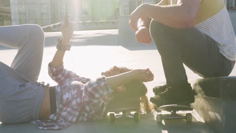 happy caucasian female and male friends using smartphone at a skatepark