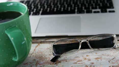 coffee mug, laptop, spectacle on wooden plank