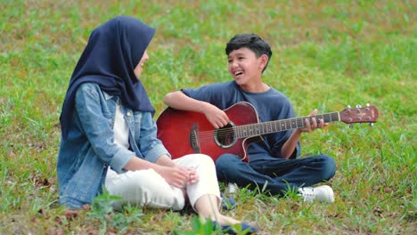 happy asian teenage friends having fun singing and playing guitar