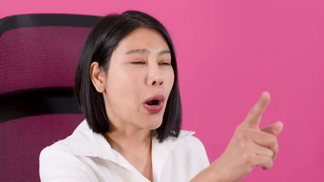 ピンクの背景の前で、笑顔のアジア人女性が話したり身振り手振りをしたりしているミディアムショット。