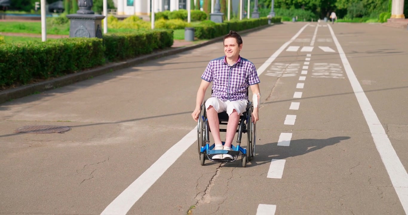 Lächelnder junger Mann sitzt an einem sonnigen Tag im Rollstuhl