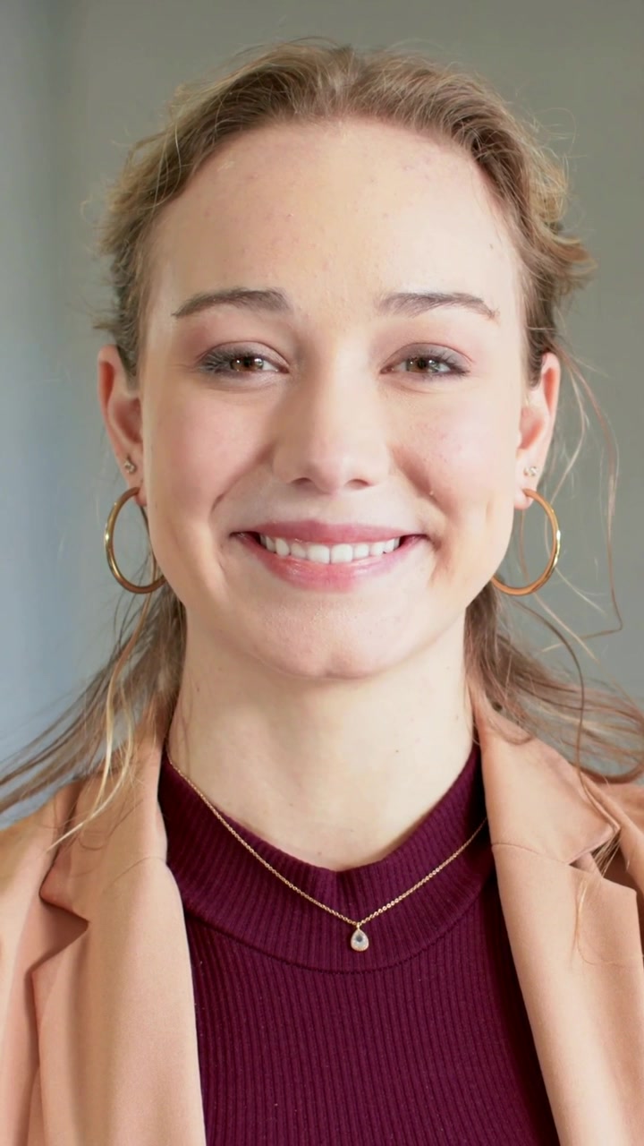 Vertical video: Camera starting, woman shifting to smile in office for portrait, in blazer, hoops