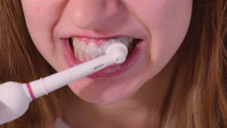 a lady is using an electric toothbrush to brush her teeth - close up