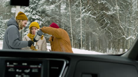 cheerful friends drinking hot tea in a snowy forest during a winter road trip 1