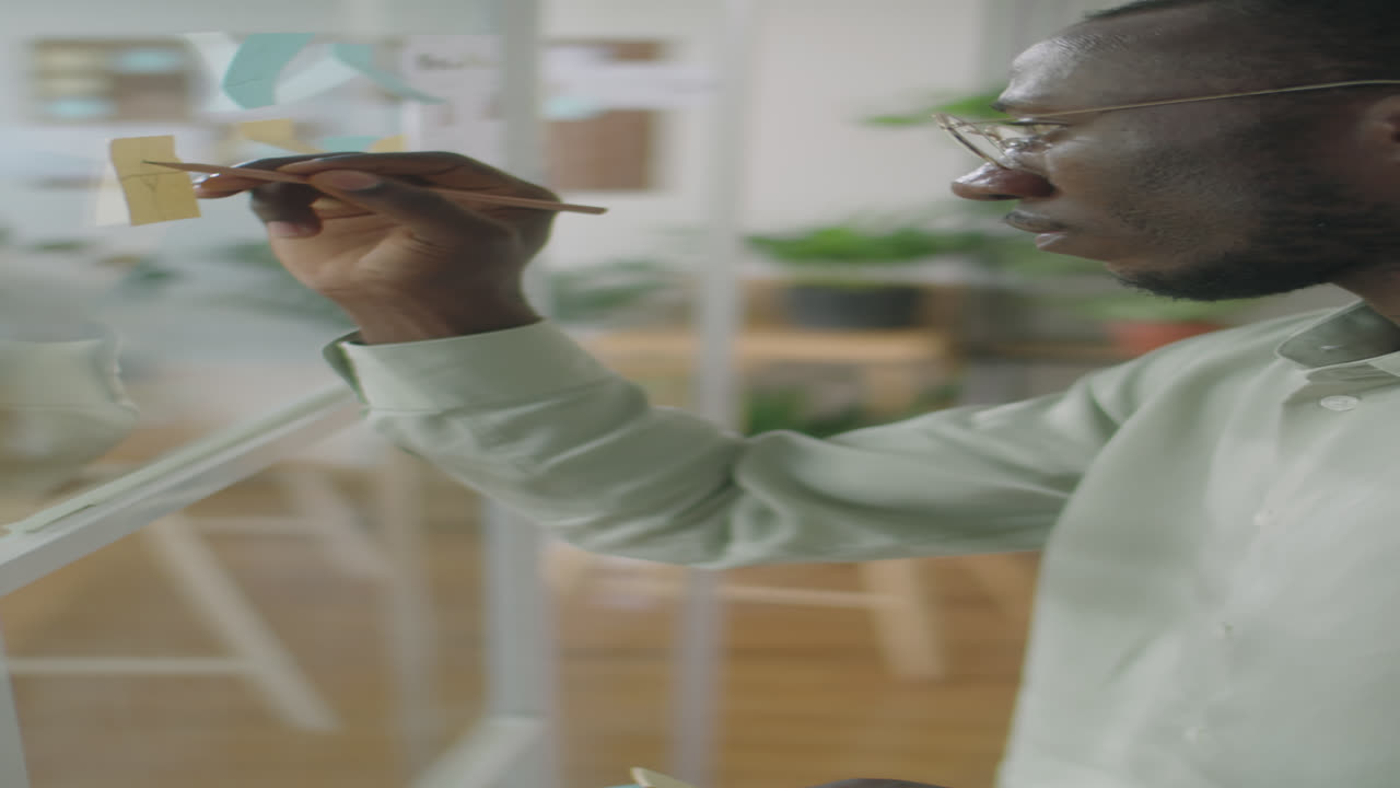 African American Businessman Writing on Sticky Notes on Glass Wall