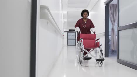african american female doctor running with wheelchair in hospital corridor, slow motion