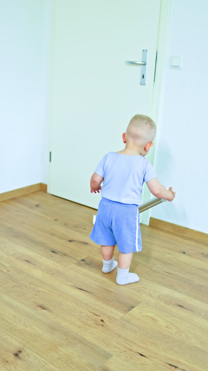 Cute 2 year old boy vacuuming the floor with a cordless vacuum cleaner. Toddler helps with cleaning the apartment. Child does housework and cleans his room