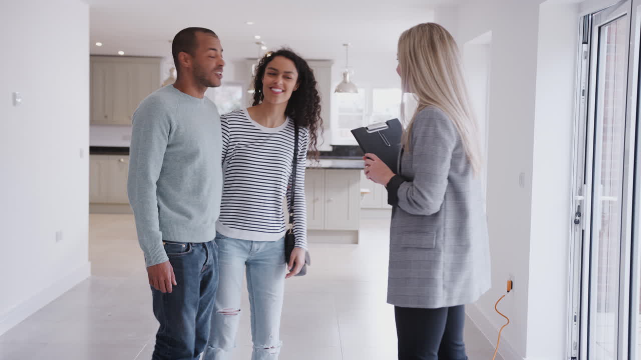 Female Realtor Showing Couple Interested In Buying Around House