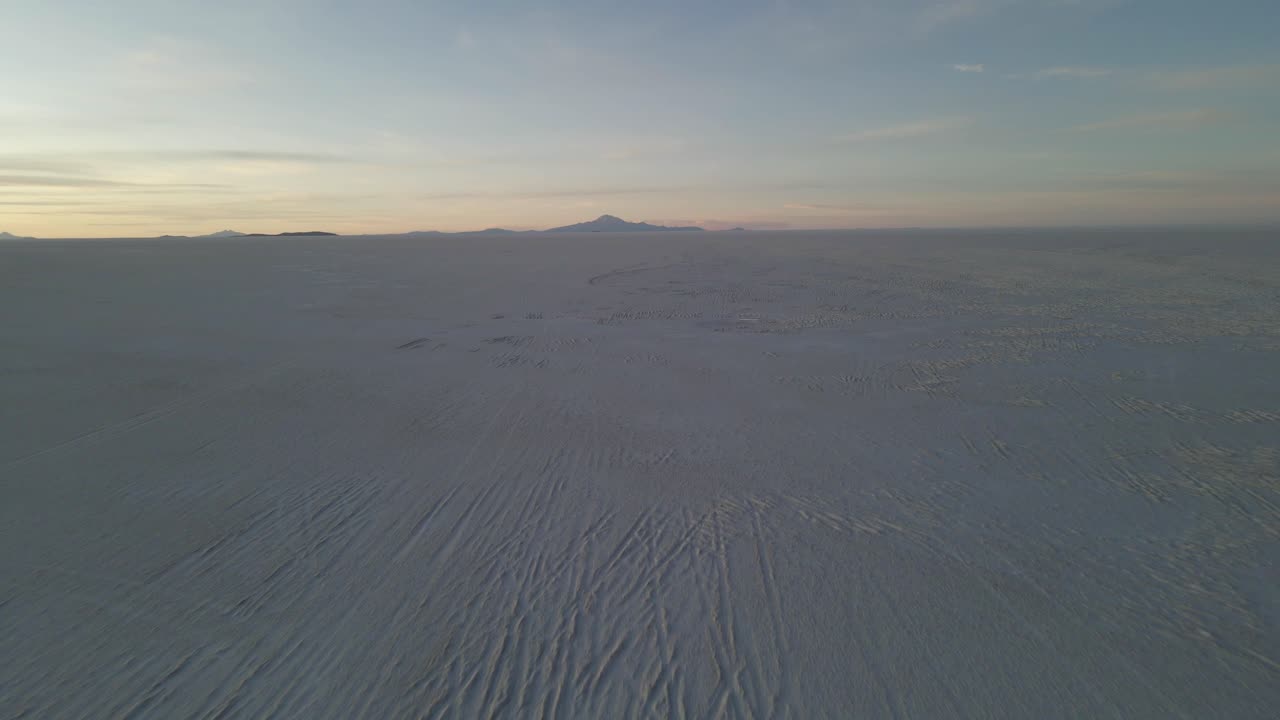 Drone dolly over reflected sky on Uyuni salt flat crossing surreal dry lake bed with tire tracks