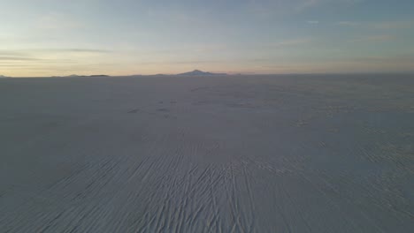 drone dolly over reflected sky on uyuni salt flat crossing surreal dry lake bed with tire tracks
