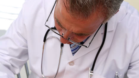 Doctor-writing-on-prescription-pad-at-his-desk