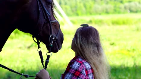 una joven rubia con una camisa a cuadros da un paseo con su caballo. una mujer se comunica con un caballo. noche soleada de verano.