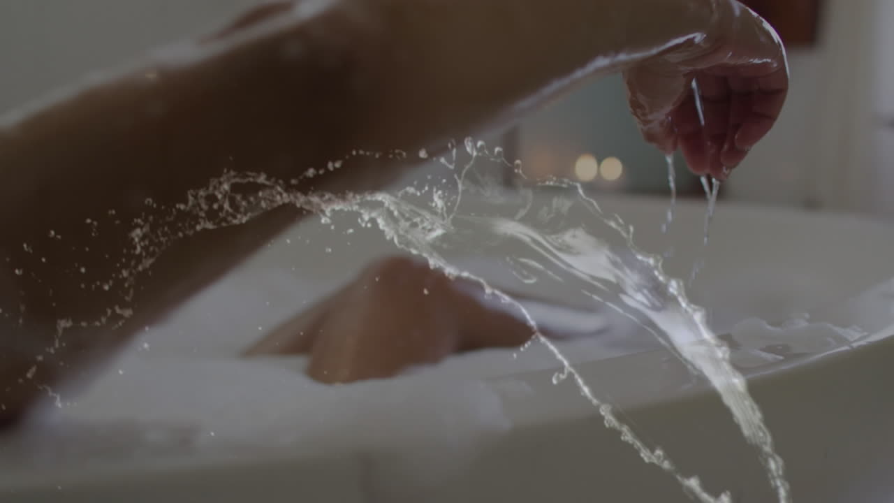 Animation of water splash over happy african american woman relaxing in bath tub