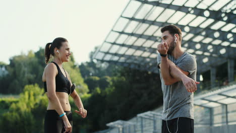 young jogger couple exercising and warming up hands and shoulders in the stadium in summer