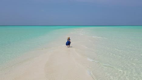 young girl wearing a long blue dress running barefoot on a surreal white sandbank with turquoise waters of indian ocean, maldives drone shot on a clear sunny day