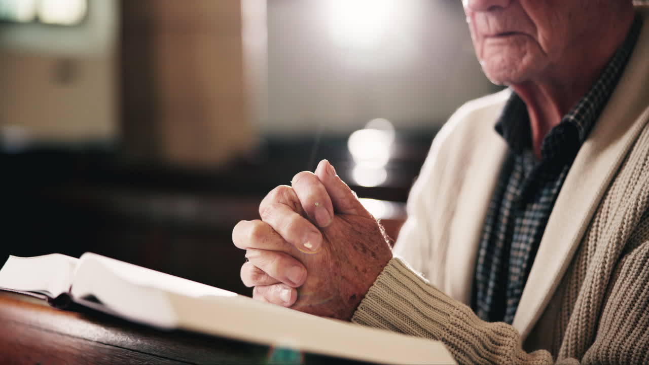 An elderly man is praying over an open bible