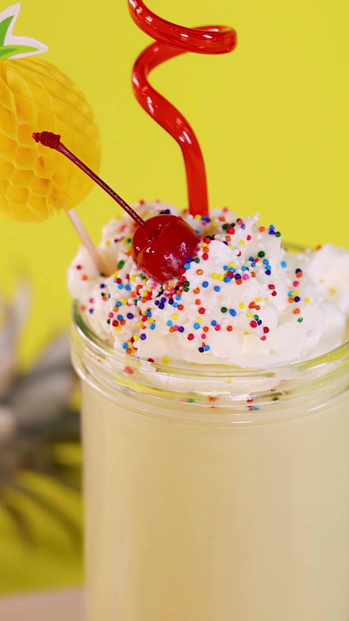 Primo piano di frappè tropicale all'ananas guarnito con panna montata, ciliegia, codette colorate e cannuccia riccia