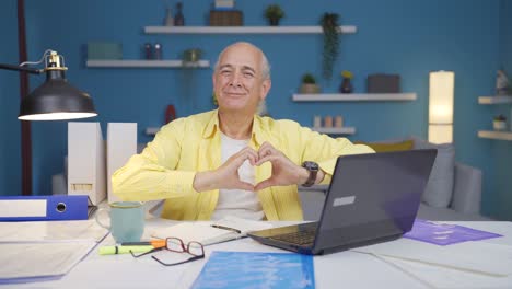 home office worker old man makes heart symbol looking at camera.