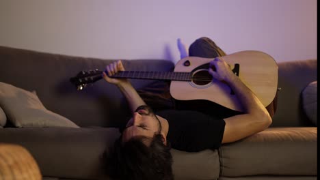 hombre triste tocando la guitarra mientras está acostado en el sofá