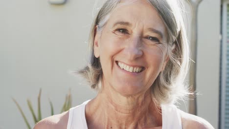 Portrait-of-happy-unaltered-senior-caucasian-woman-smiling-in-front-of-wall-and-plants,-slow-motion