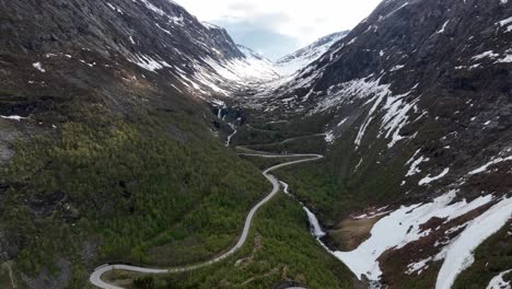 curvy winding road strynevegen leading to old strynefjellet mountain crossing - norway springtime aerial with beautiful waterfall close to road