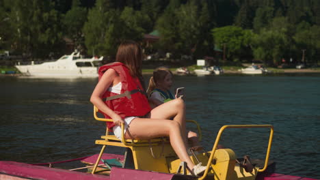 mother and little child ride catamaran on lake. girl looks at mobile phone reviewing photos slow motion side view. family vacation at resort