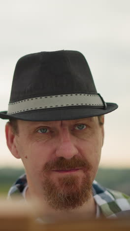 an artist wearing a black hat intensely focused on an unseen task, with mosquitoes visibly flying around his head. a partially visible board in front suggests he's working on something important