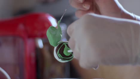 woman decorating a cake pop with green coloured melted chocolate