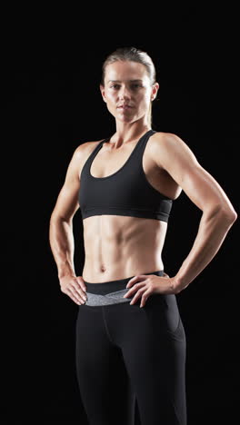 vertical video: caucasian female athlete posing, black background