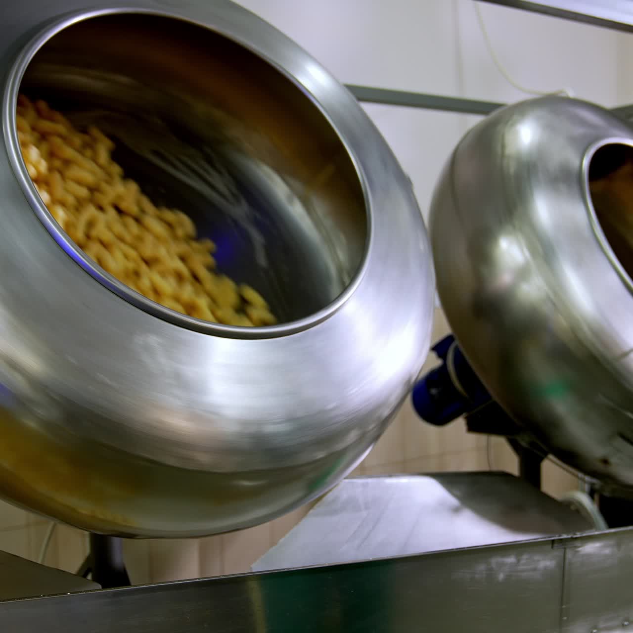 Two metal rotating tanks filled with sweet snacks. Corn sticks being covered with sugar syrup from a special disperse device