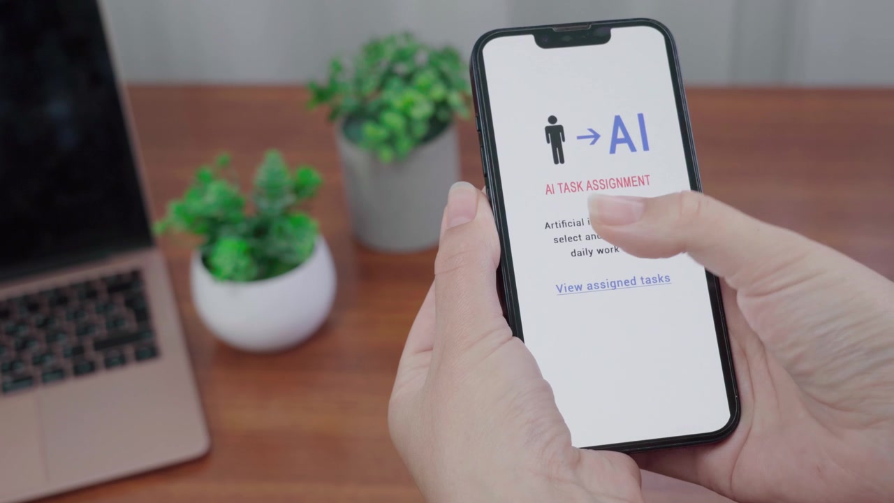 Hænder holder en smartphone, der viser en skærm for AI-opgavetildeling, hvor kunstig intelligens udvælger og tildeler daglige arbejdsopgaver.