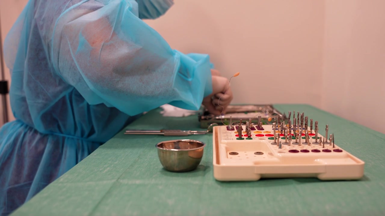 Inquadratura media di un assistente dentista che indossa una tuta DPI e organizza con cura gli strumenti e il materiale per il medico per un impianto.