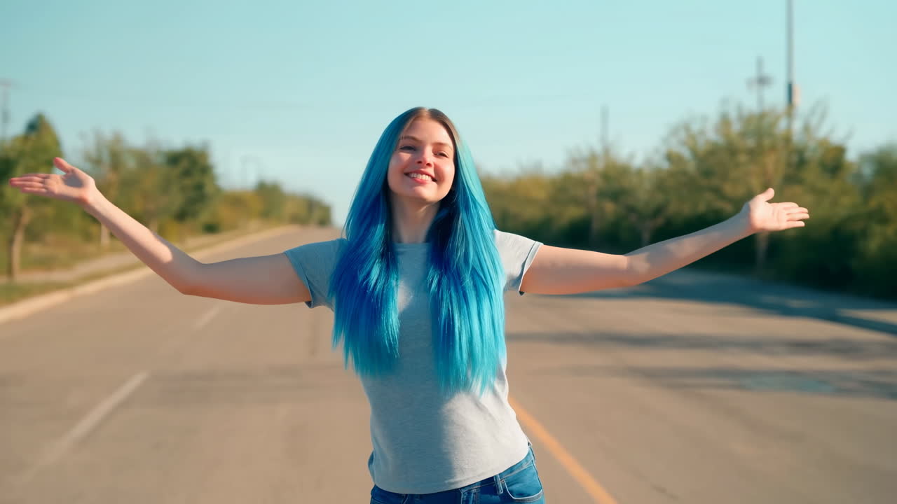 Joven feliz con cabello azul de pie en una carretera vacía