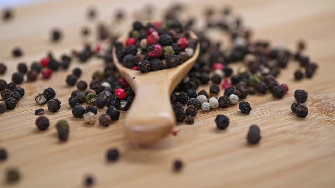 Spinning mixed peppercorns in wooden spoon on cutting board