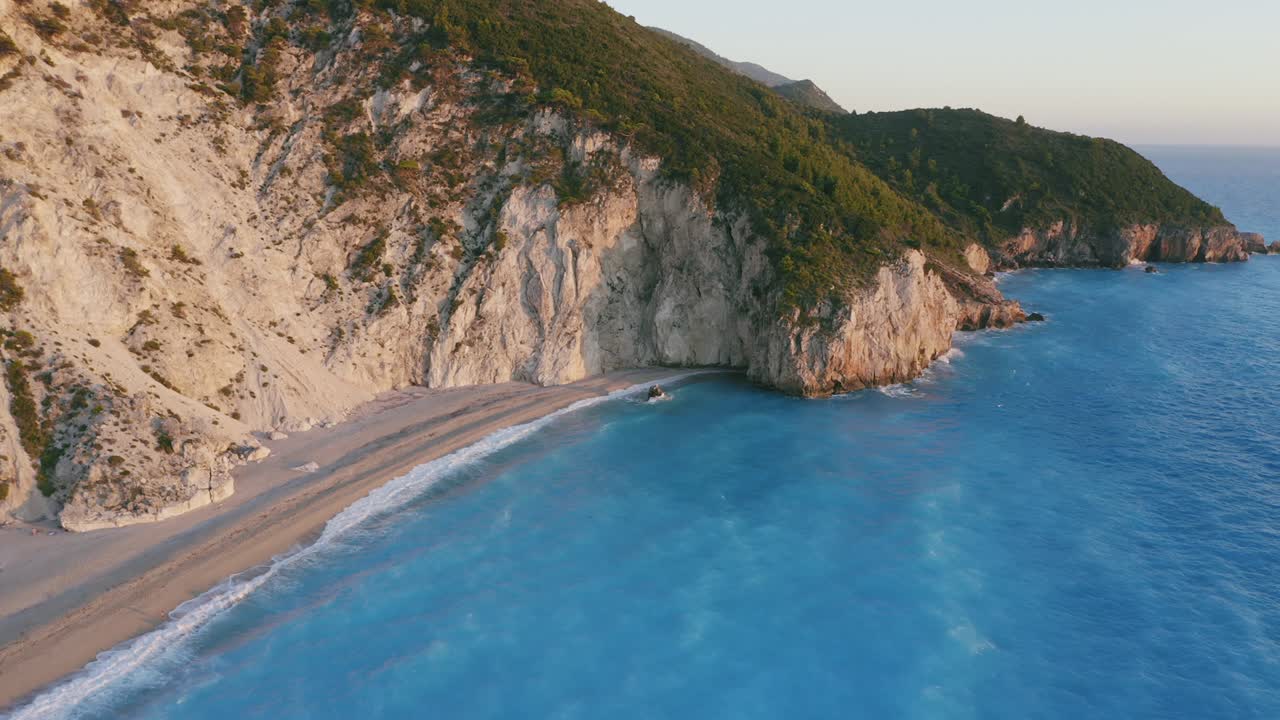 Aerial circle motion around beautiful Milos beach of Lefkada, Ionian island, Greece. Sunset golden sunlight and pristine waves breaking the turquoise blue sea on the shore