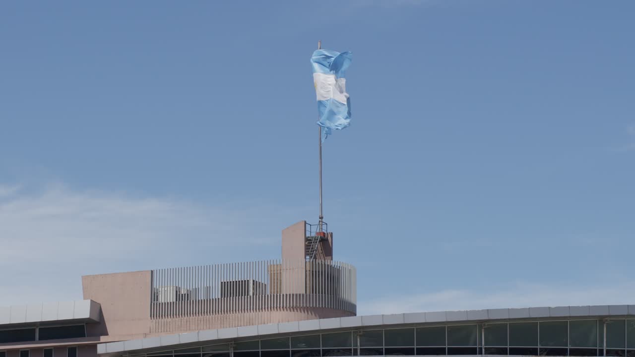 Images panoramiques du drapeau argentin flottant fièrement à Punta del Centinela par une journée ensoleillée, capturant l'esprit patriotique au milieu du paysage pittoresque