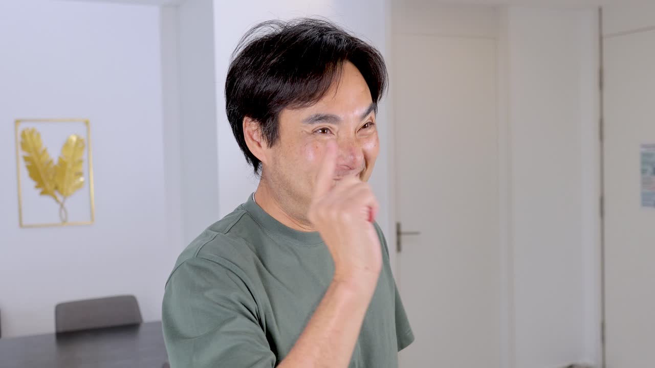Confident Asian man smiles and points finger gun gesture in bright, modern indoor setting