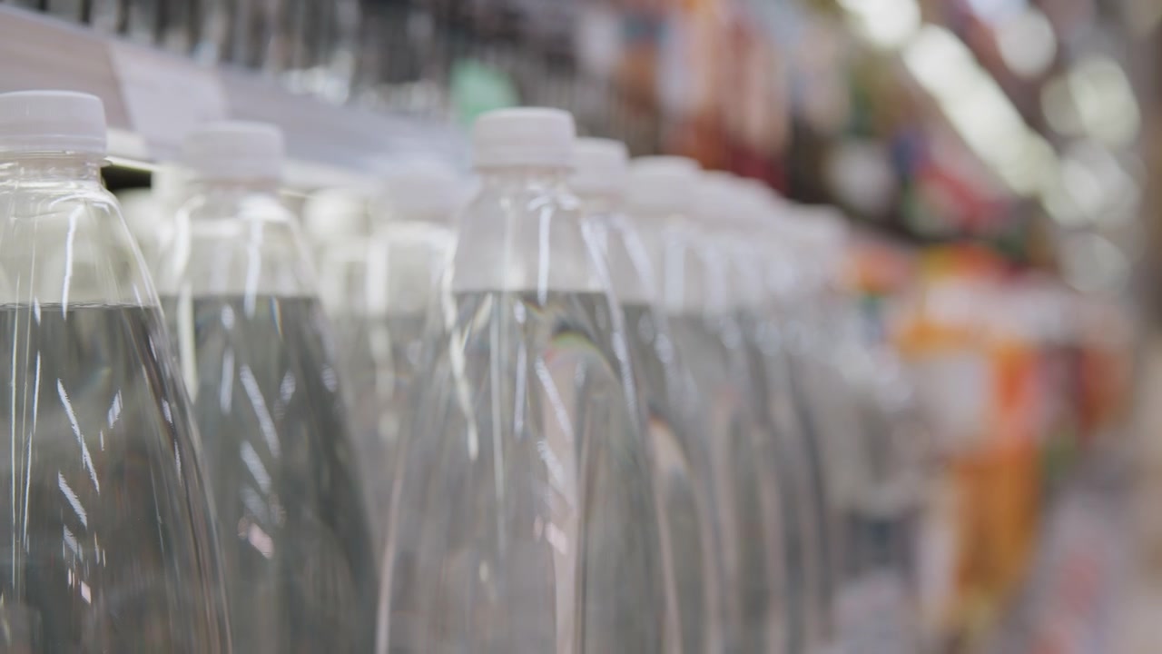 Mano che controlla l'etichetta e il tappo di una bottiglia d'acqua, ispezione ravvicinata nel corridoio del supermercato, focus sul codice a barre e sull'imballaggio, acquirente che valuta qualità e sostenibilità, sfondo attenuato con negozio soft