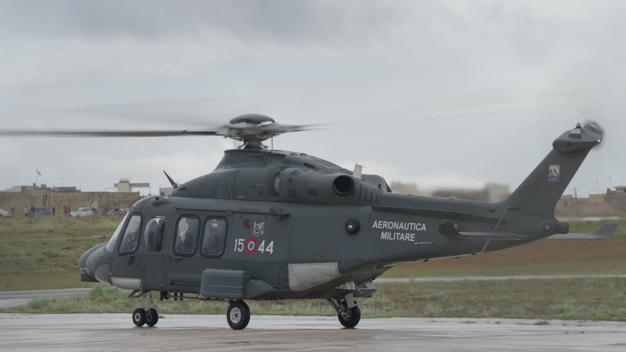 駐機場にいる、ローターが回転しているイタリア空軍の軍用ヘリコプター。