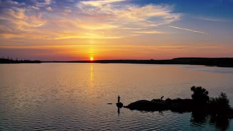 flying over the evening river and some people standing on a stone in water. golden sun setting on the natural water background. silhouette of a fisherman at sunset.