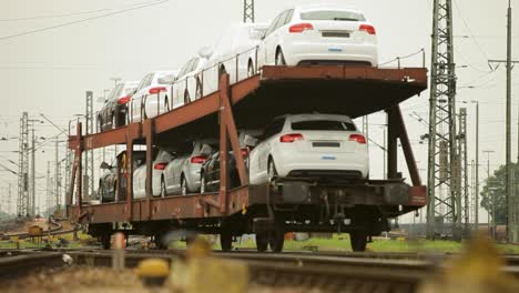 vagones nuevos transportados por ferrocarril en un vagón de tren de mercancías de varios niveles en un patio ferroviario