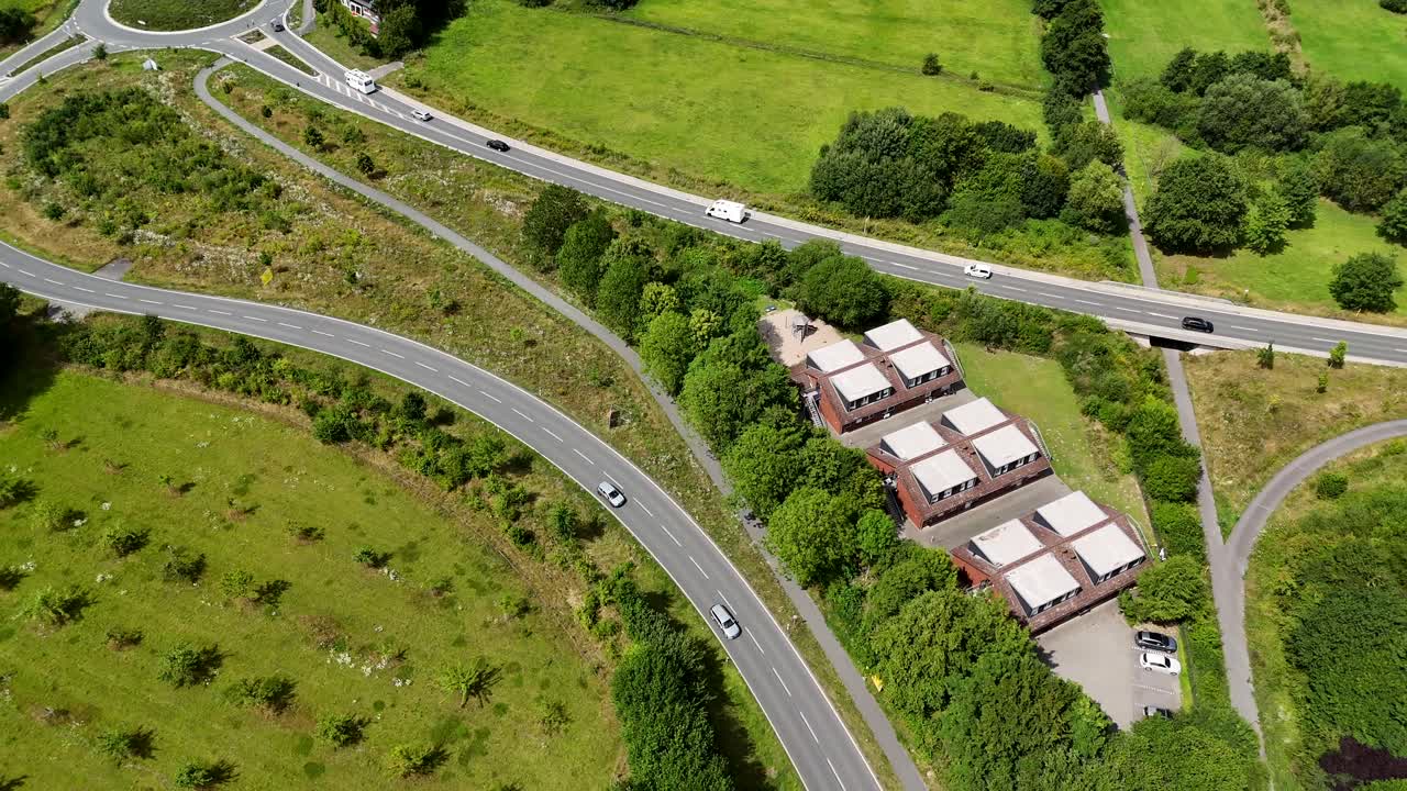 New Build roundabout and interstate roads in rural area of America. Sunny day with green grass fields. Aerial top down. Solar panels on roof of homes. Driving cars on streets at daytime