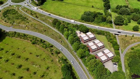 new build roundabout and interstate roads in rural area of america. sunny day with green grass fields. aerial top down. solar panels on roof of homes. driving cars on streets at daytime