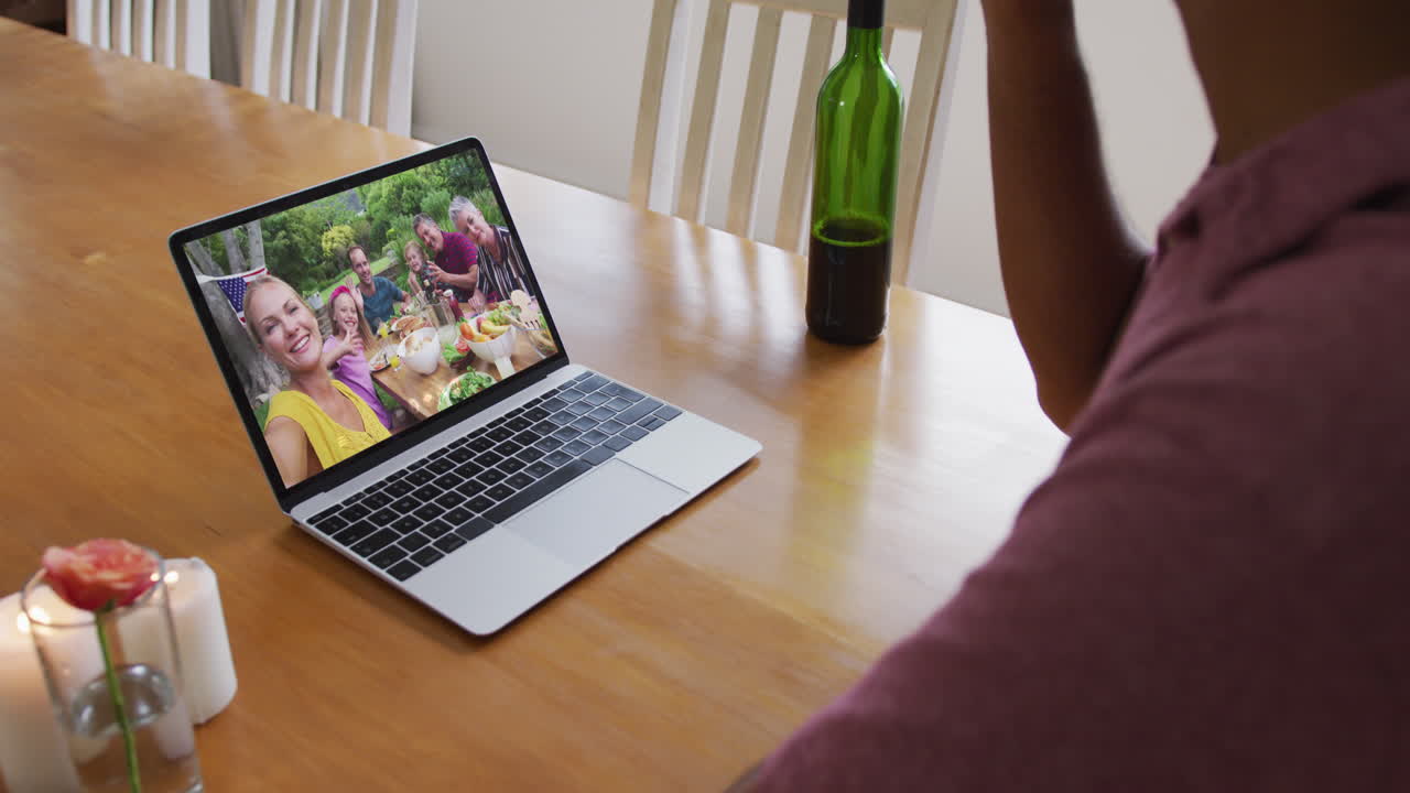 Busto di uomo afroamericano che beve vino durante una videochiamata al laptop a casa.