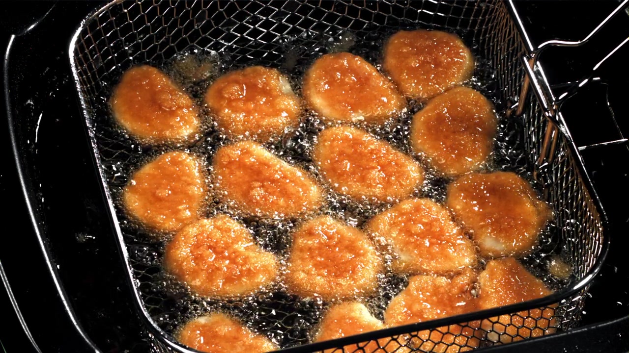 フライヤーの熱い油で揚がるチキンナゲット