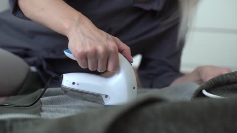 wireless device for cleaning knitted fabrics from lint. the woman is removing the lint from the sweater.