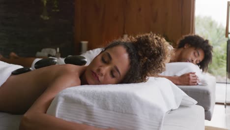 video of relaxed diverse couple having hot stone massage treatment at health spa