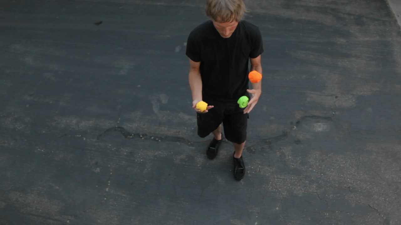 한 남자가 손과 발을 모두 사용하여 세 가지 색깔의 공을 저글링합니다.