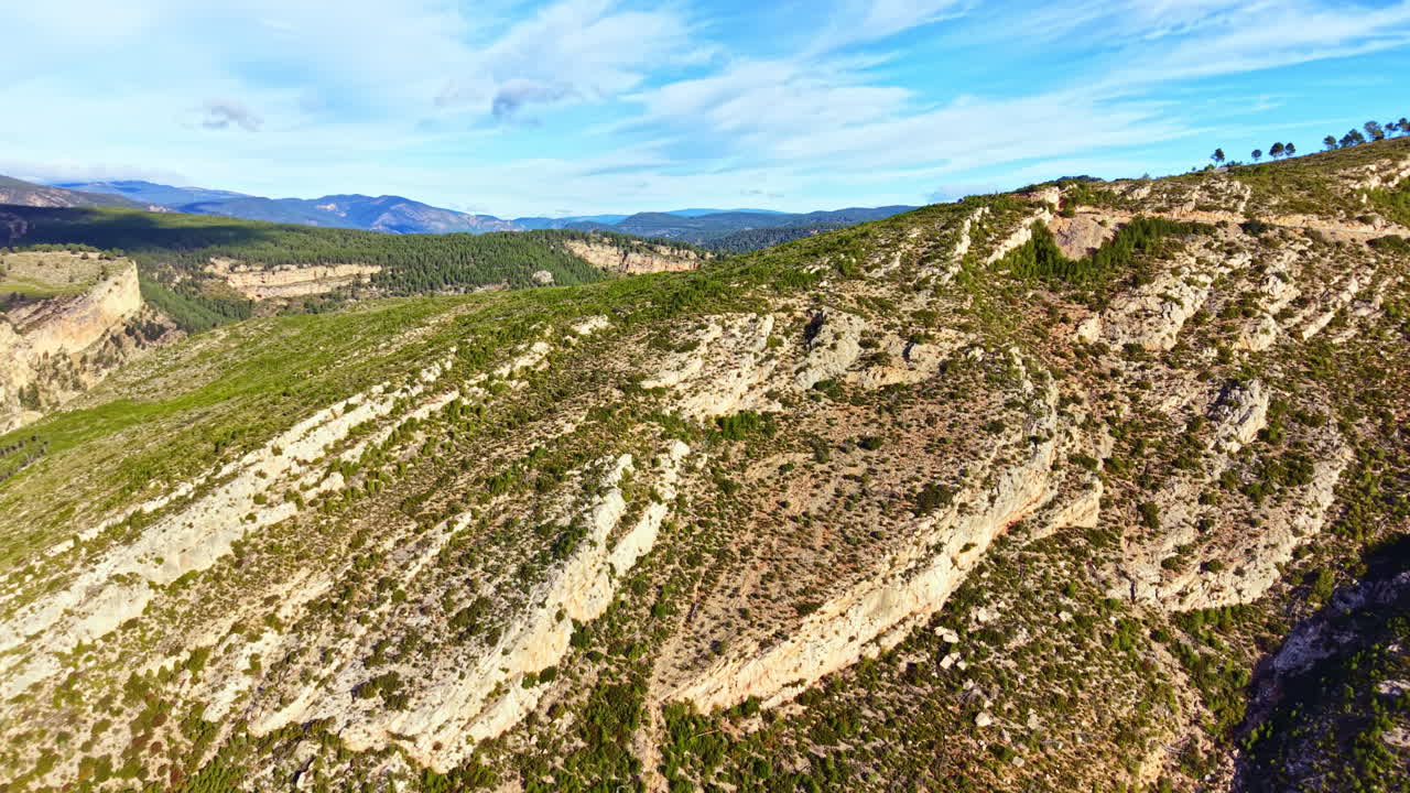 Paesaggio montano con colline verdi e cielo blu di giorno, in un ambiente naturale caratterizzato da formazioni rocciose e montagne distanti.