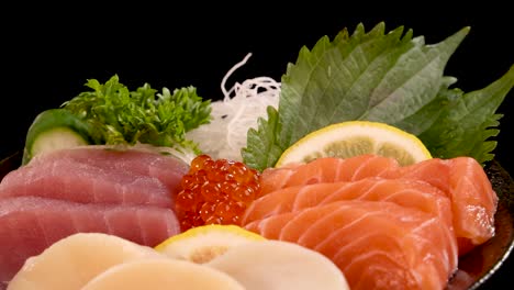 a vibrant japanese sashimi platter with salmon, tuna, scallop, and salmon roe rotates slowly against a black background under bright, even lighting